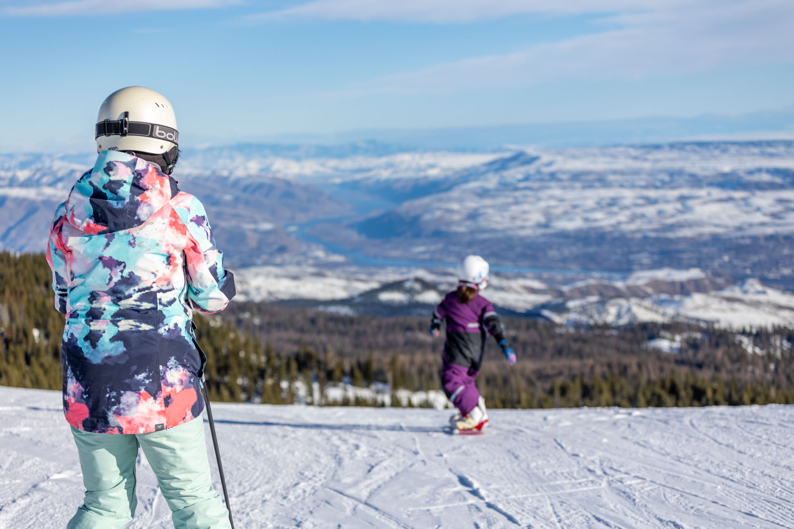 Young snowboarder at Mission Ridge in front of adult on groomed run with valley view below