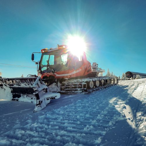 Red snowcat leaving tracks in the snow with sun behind