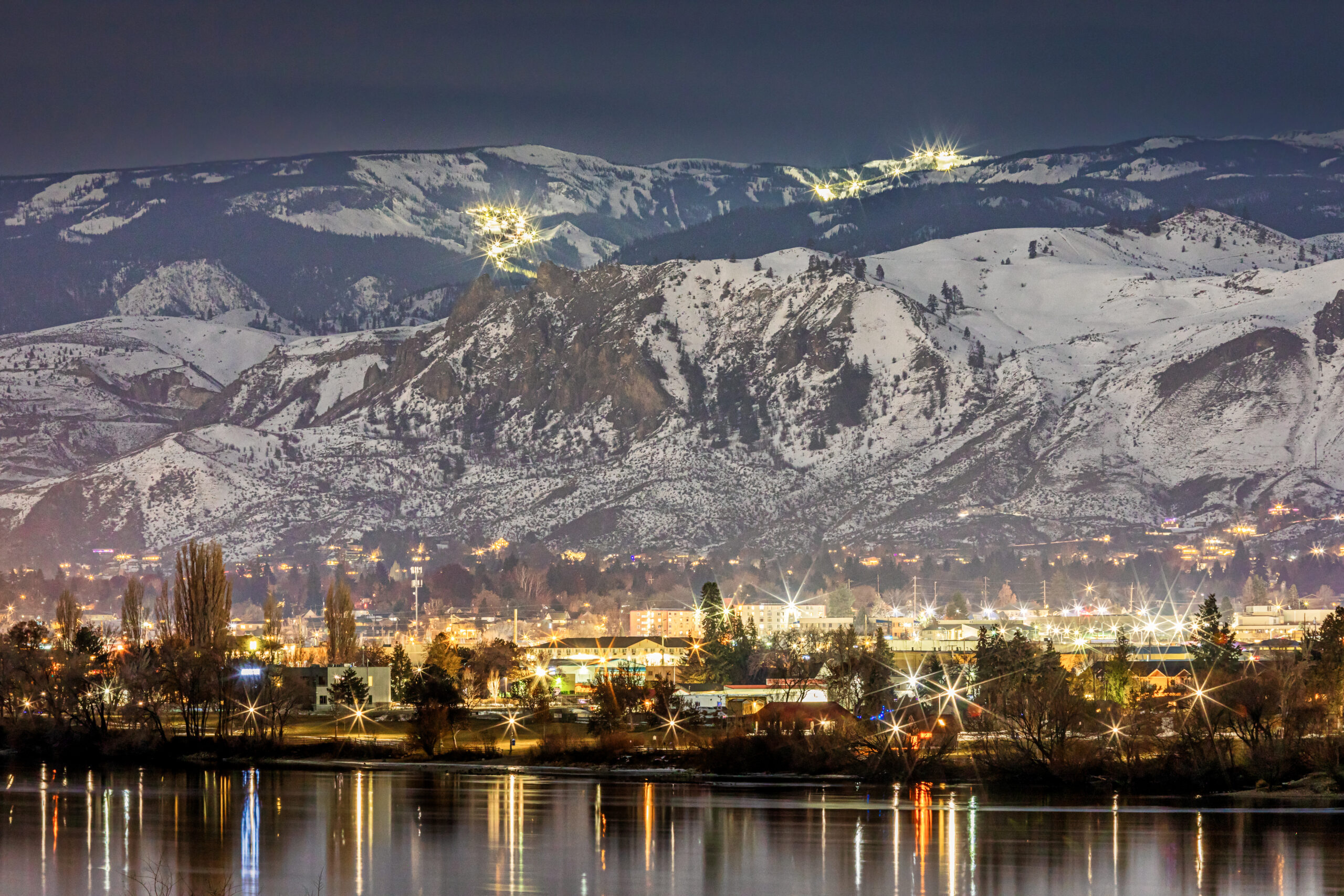 View of Mission Ridge and Wenatchee at night covered in snow from across the Columbia River.