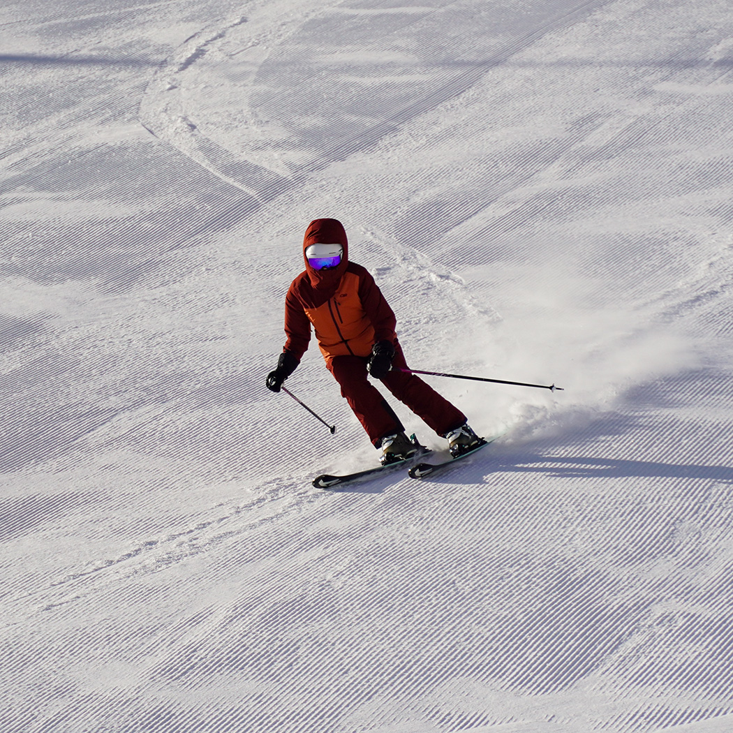 Skier in red jacket and red pants carving turn on fresh corduroy