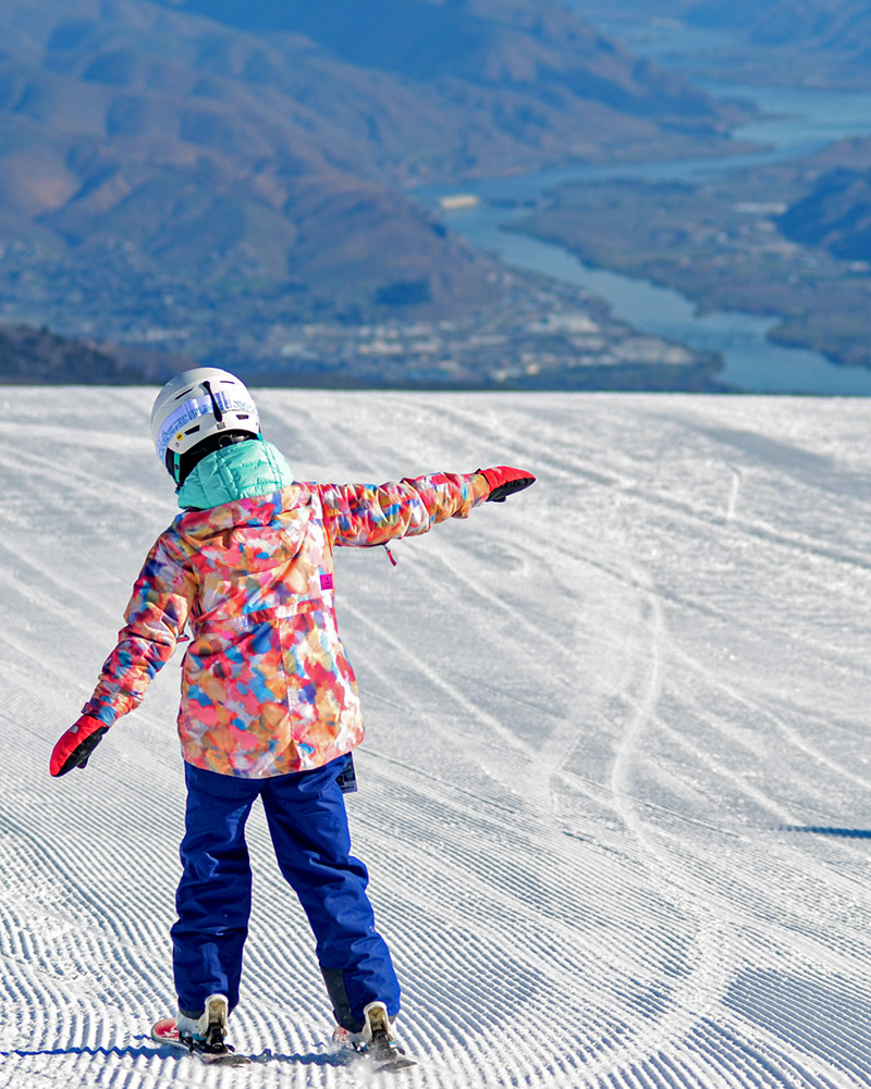 Child at Mission Ridge in colorful jacket with arms outstretched like an airplane with valley view below