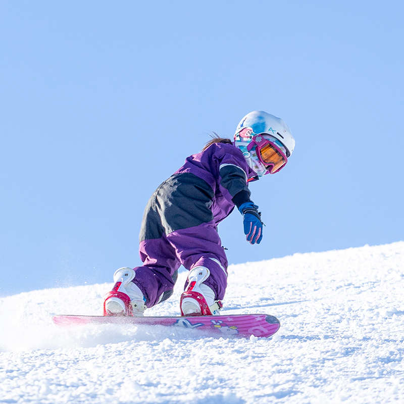 Young snowboarder in purple making toeside turn