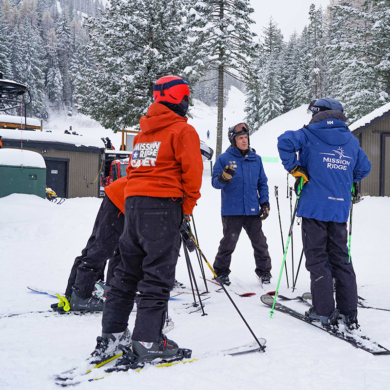 ski instructors in blue jackets and Cadets in orange jackets standing in circle discussing technique