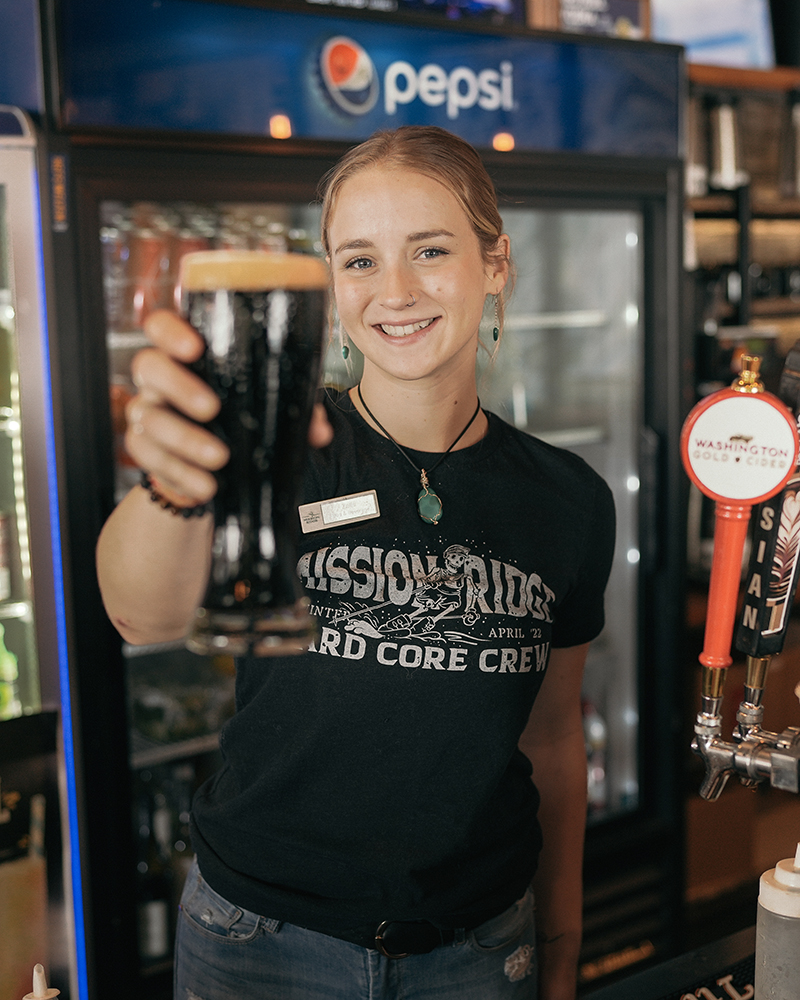 Bartender in black shirt holding up a glass of dark beer