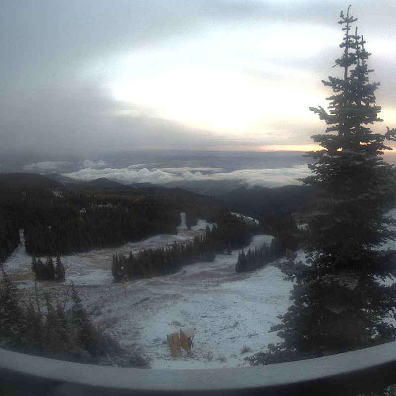 Early morning view from the Sunspot webcam of light snow on the ground with valley view below