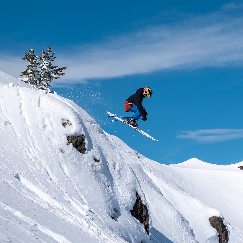 Young skier in black jacket and blue pants going off jump