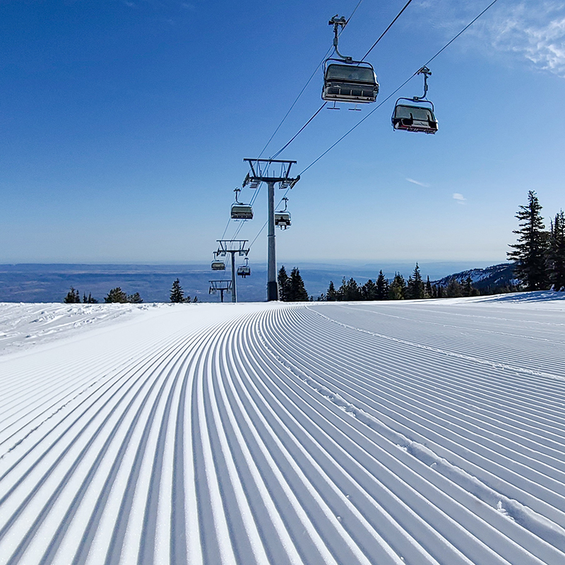 Close up of freshly groomed snow with chairlift behind