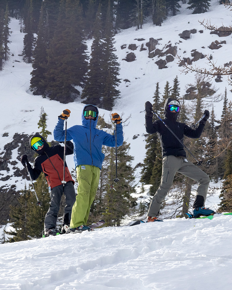 Three skiers raising their hands in the air with ski poles smiling