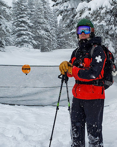 Ski Patroller in red and black standing in front of gate with orange closed sign