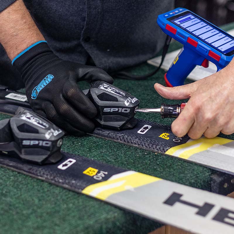 Close up of technicians hands adjusting ski binding with screw driver