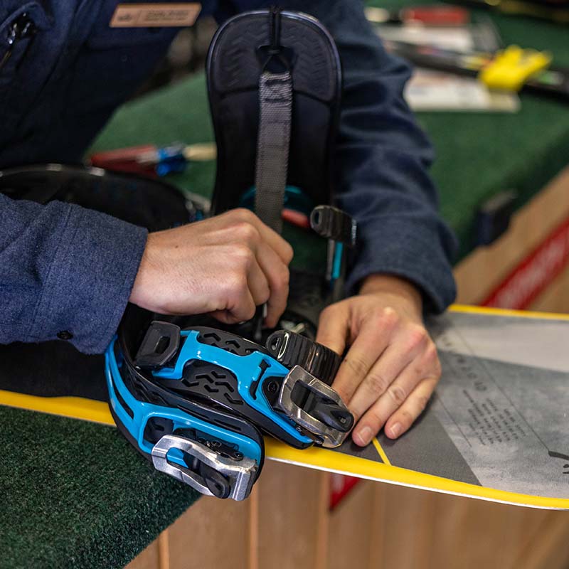 Close up of technicians hands adjusting blue snowboard binding
