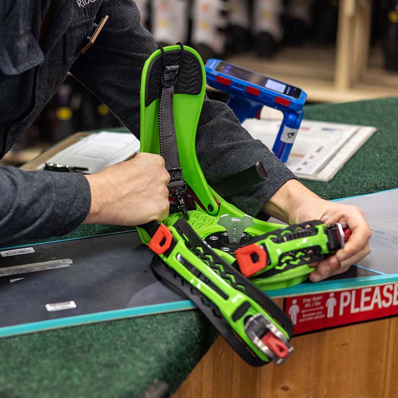 Close up of technicians hands adjusting green snowboard binding
