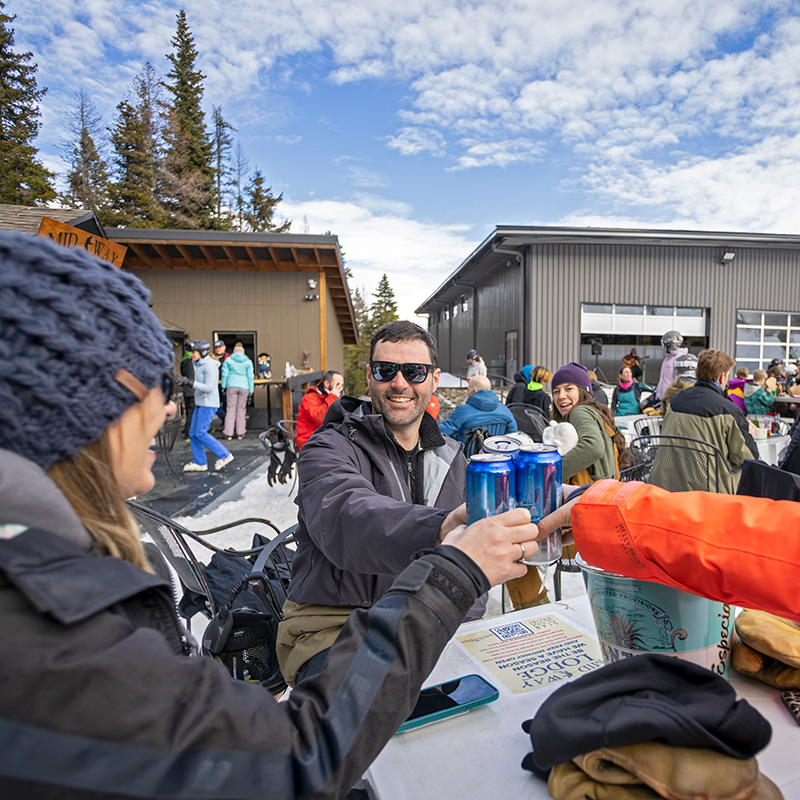 Group sitting around a table at Mission Ridge's Midway lodge smiling cheersing blue canned drinks