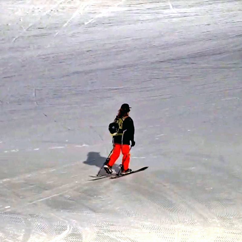 Snowboarder in black jacket and orange pants skinning uphill with splitboard