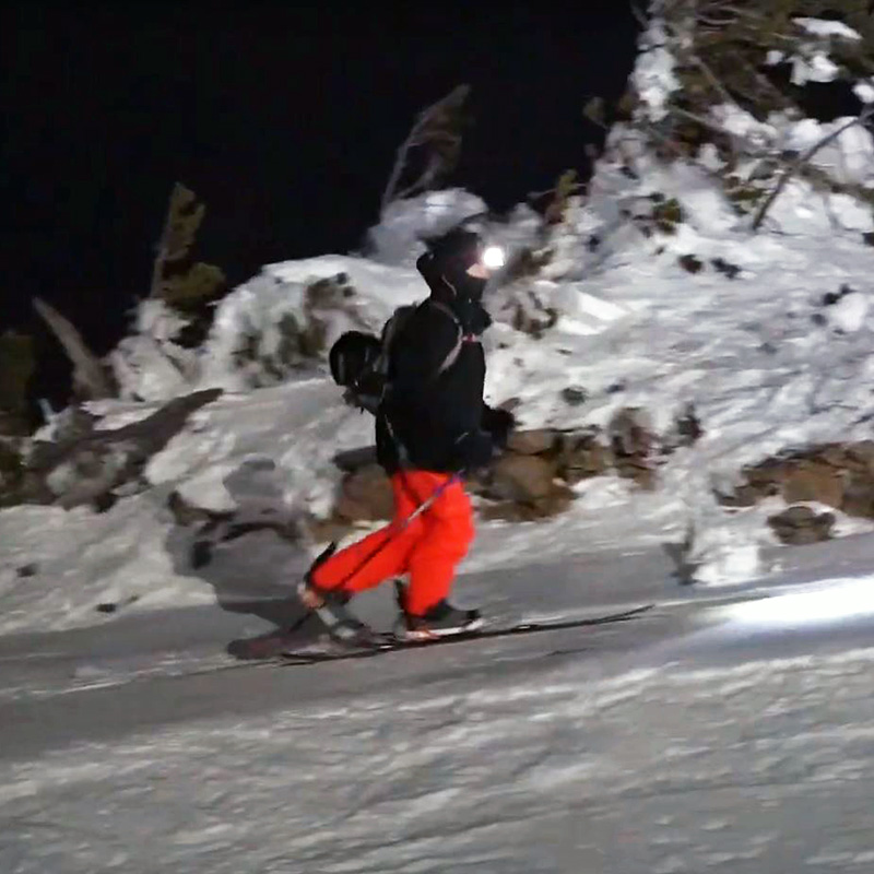 Snowboarder in black jacket and orange pants skinning uphill with splitboard