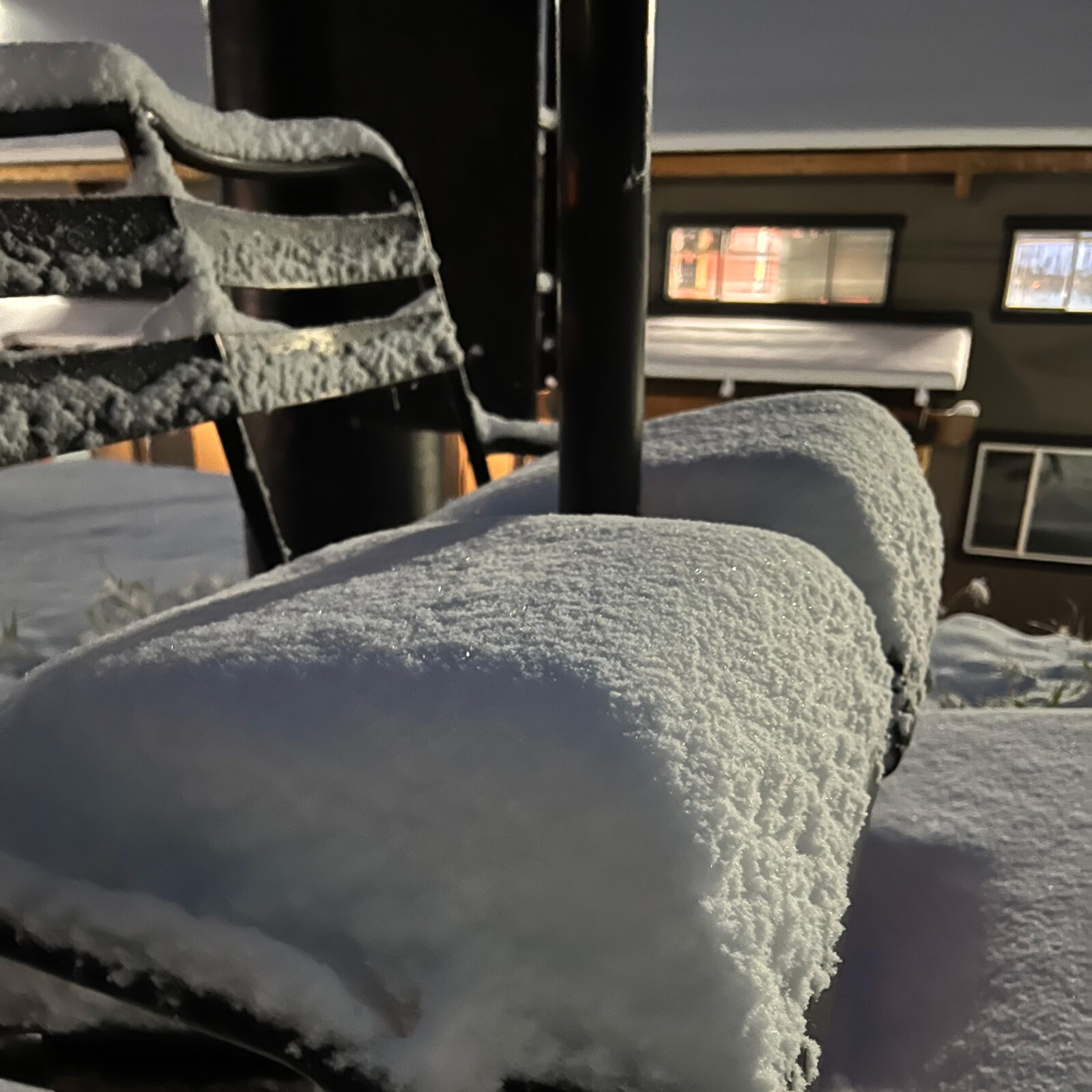 Four inches of fresh snow on a black chairlift chair in the early morning light