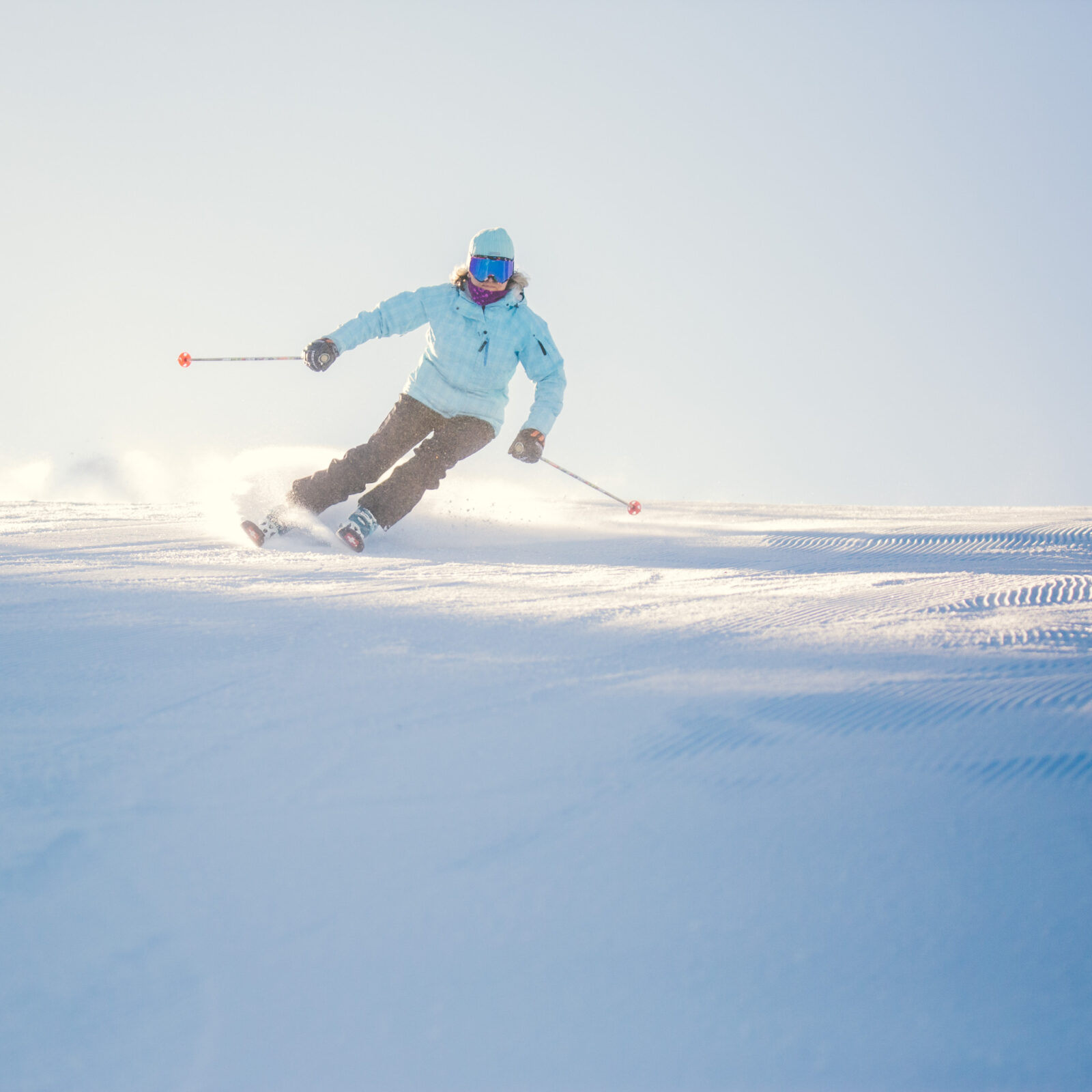 Skier in blue jacket making turn on groomed snow.