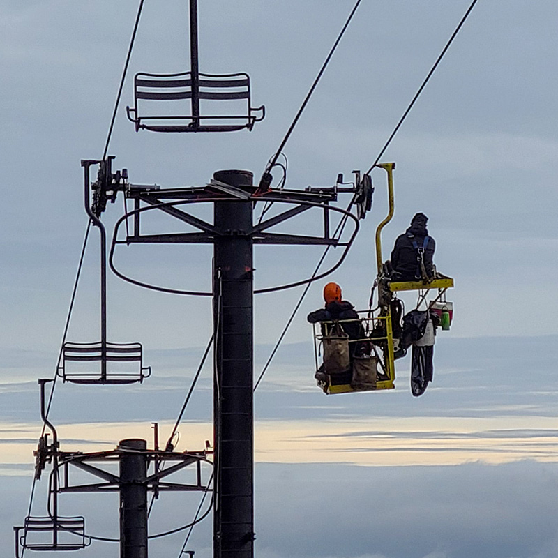 Two lift mechanics in a work basket inspecting tower machinery on a Riblet tower.