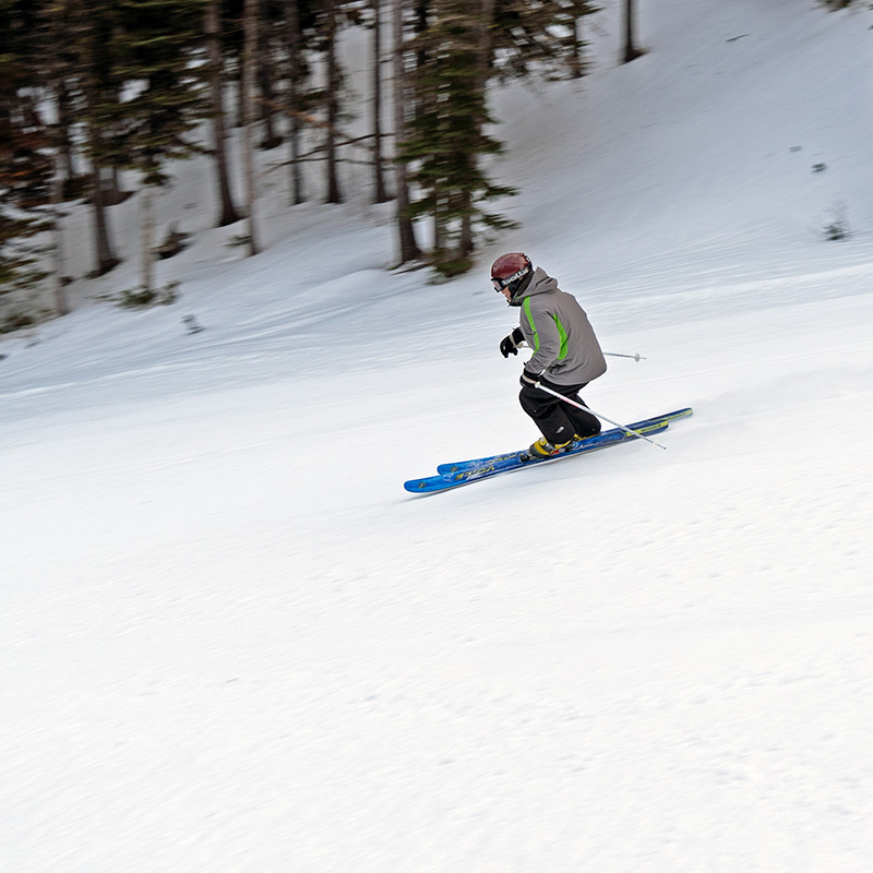 Skier in grey jacket and black pants making turn on groomed run at Mission Ridge