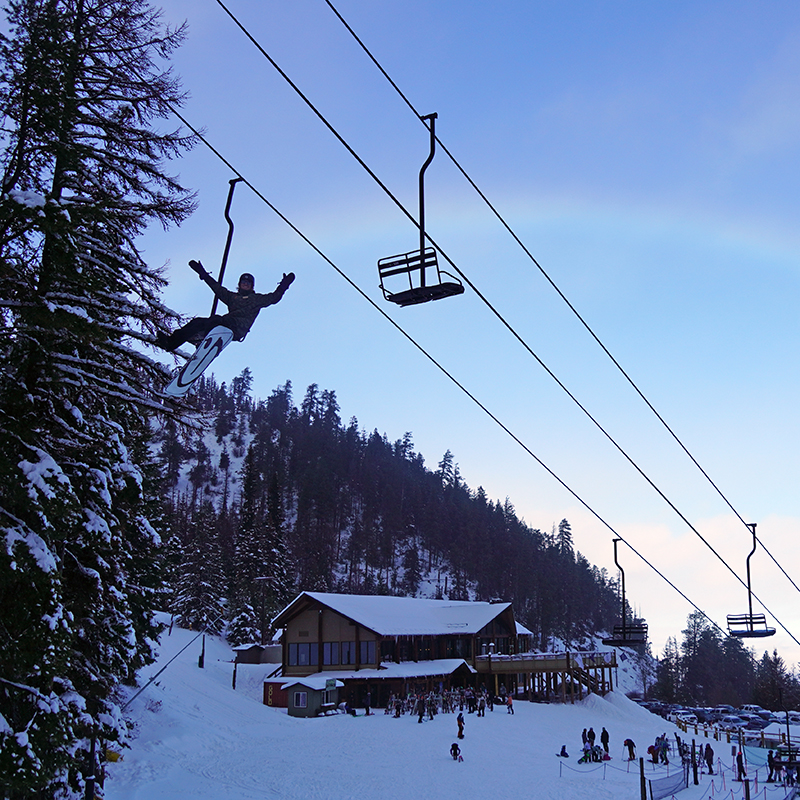 Snowboarder on chairlift waving with lodge and rainbow in background