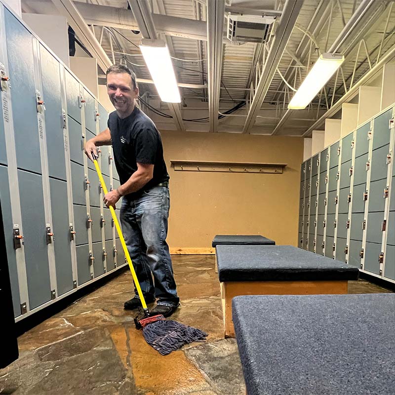 Mission Ridge Clean Team member smiling with mop in locker room