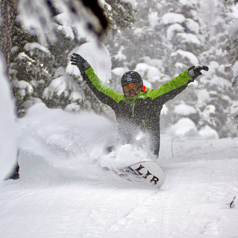 Snowboarder in green jacket making deep powder turn at Mission Ridge