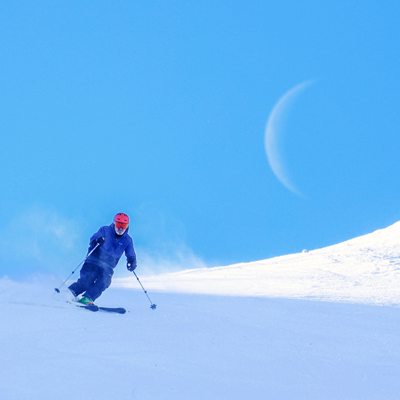 Skier making turn on groomed run with cresent moon behind