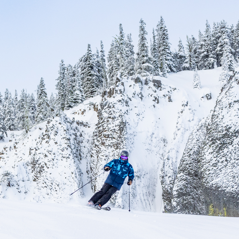 Skier on groomed run with snowy cliff background
