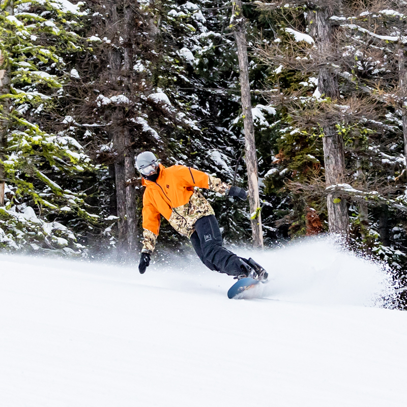 Snowboarder on toe edge throwing snow with tree background