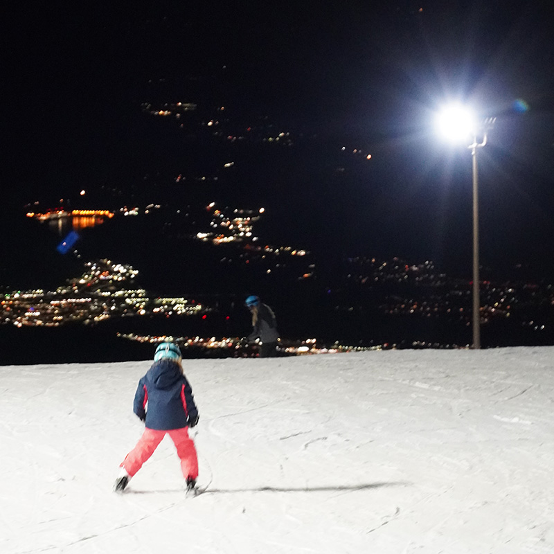 Young skier on the Sunsport run at Mission at night with the lights of the valley below.