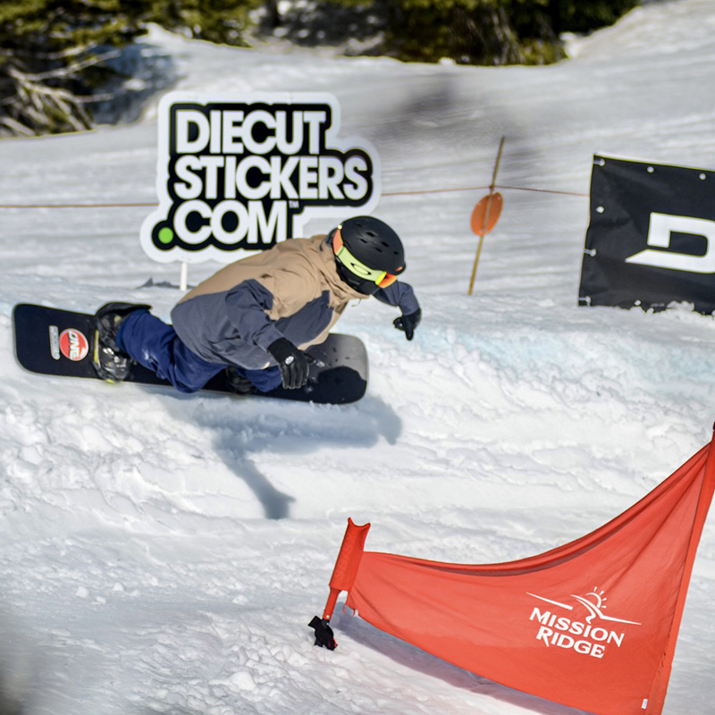 Snowboarder making turn around red snowboard race gate during the Bomber Banked Slalom at Mission Ridge.