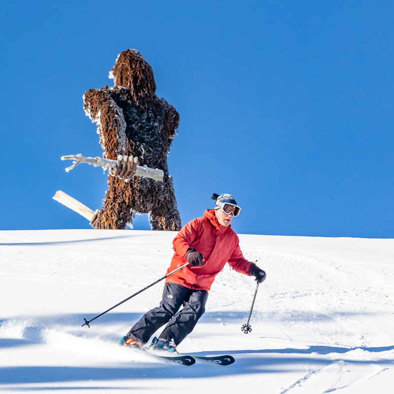 Skier carving snow in sunshine with YETI in background