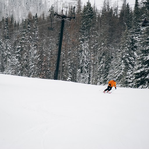 Skier wearing organe jacket goes down a groomed run with soft snow covering it on Chair 4 at Mission Ridge. There are trees with some snow covering them in the background.