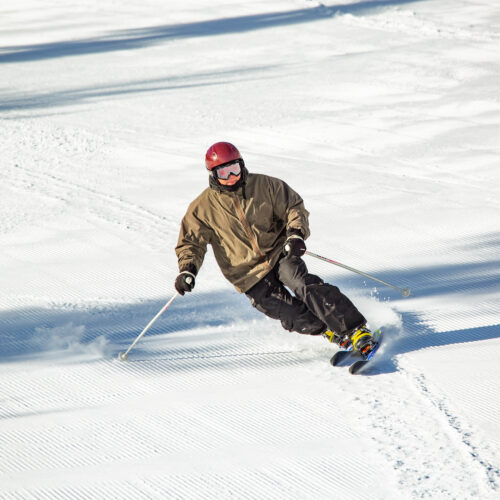 Tele skier in brown coat carving in Hidden Valley
