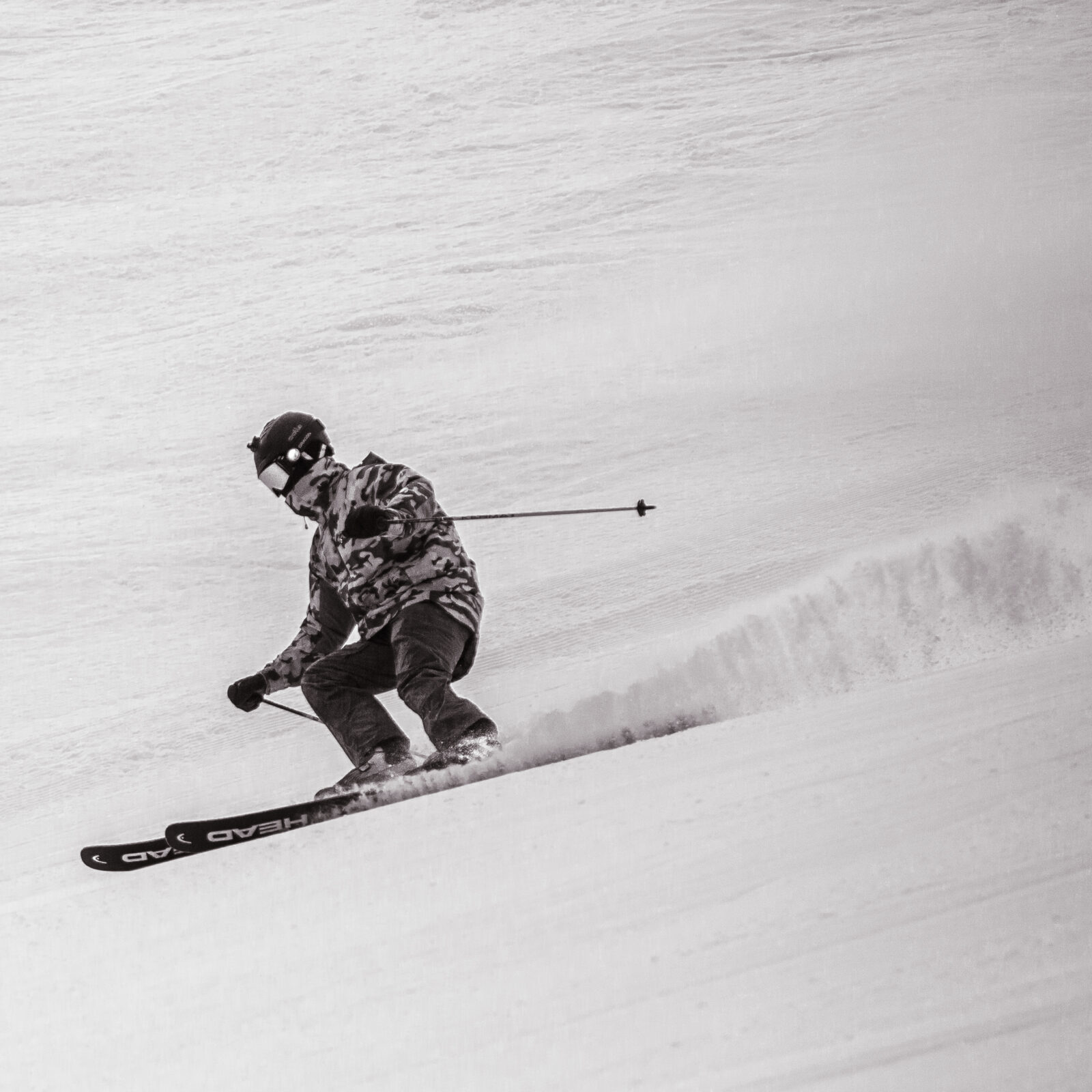 Black and white photo of skier going down Sunspot run off of Chair 2. Skier is wearing a camouflaged jacket.