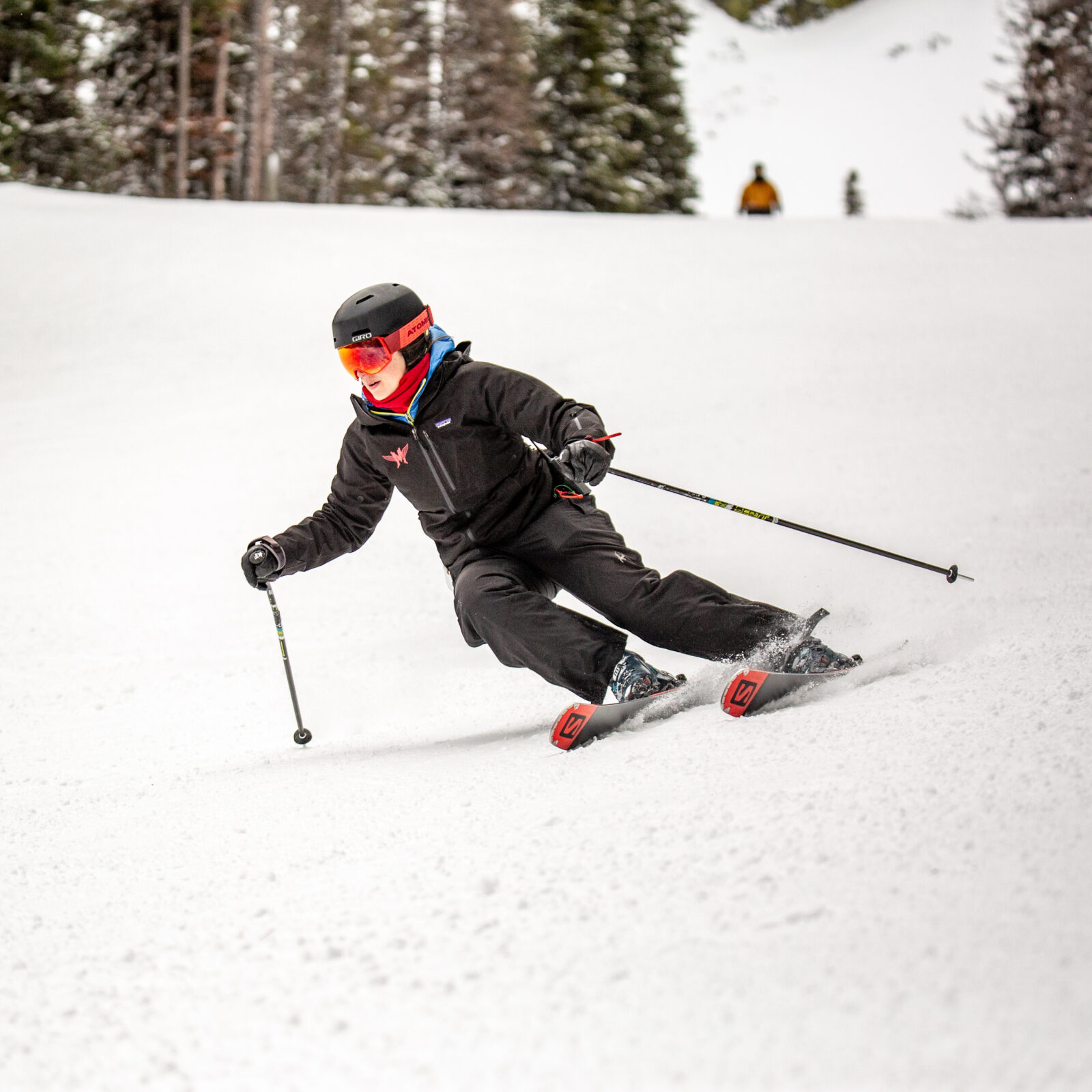 Skier carving down lower Tillikum off of Chair 3 at Mission Ridge. The skier is wearing all black and has red and orange goggles. There is some spray of snow coming of their skis.