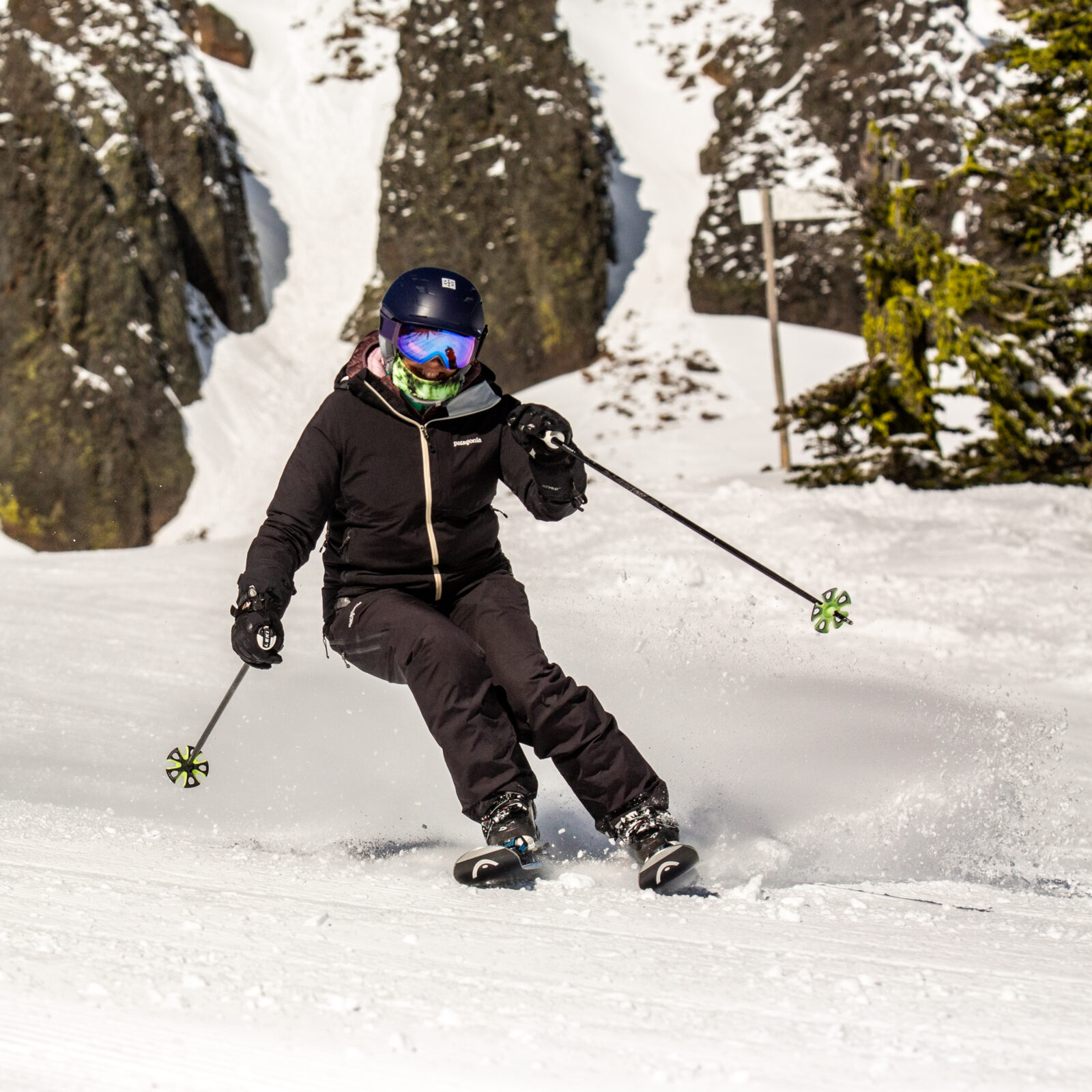 Woman skis down Hidden Valley below the Bomber Cliffs at Mission Ridge. It is a sunny day in the spring with some snow spraying off her skis.