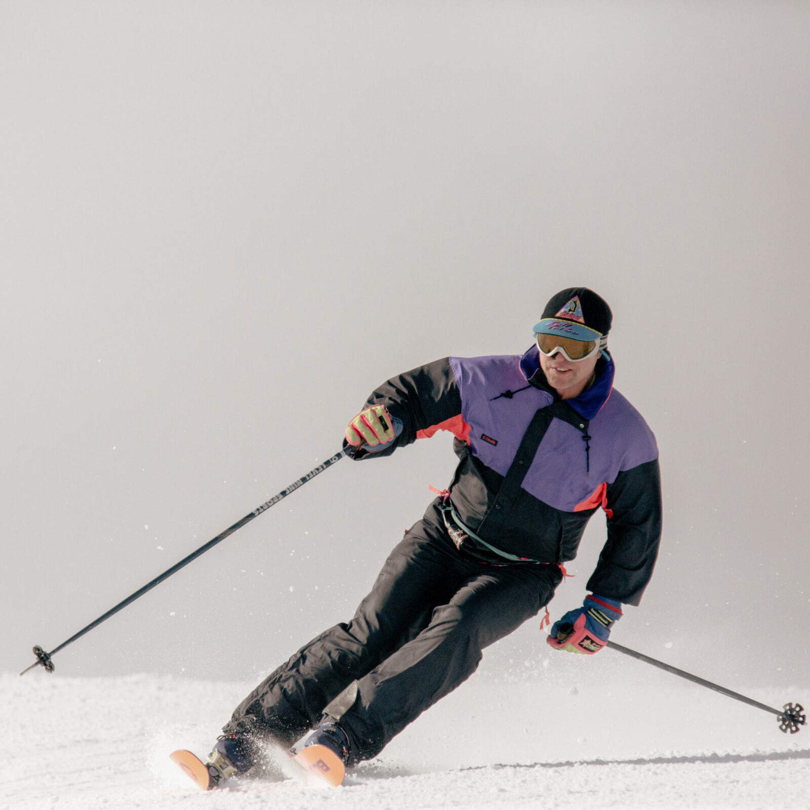 Man in 80s era retro ski gear goes down Sunspot run at Mission Ridge. This run is off Chair 2. The background is grey and white.