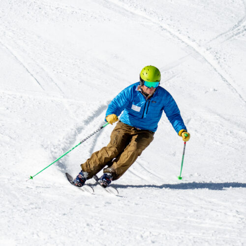 A sunny spring day where a skier goes down Nastar at Mission Ridge. He leaves tracks in the soft snow. He is wearing a blue jacket, brown pants, and lime green helmet.