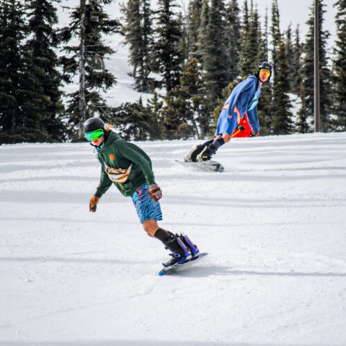 Two snowboarders go down Tumwater off of Chair 2 at Mission Ridge. The snowboarders are wearing shorts.