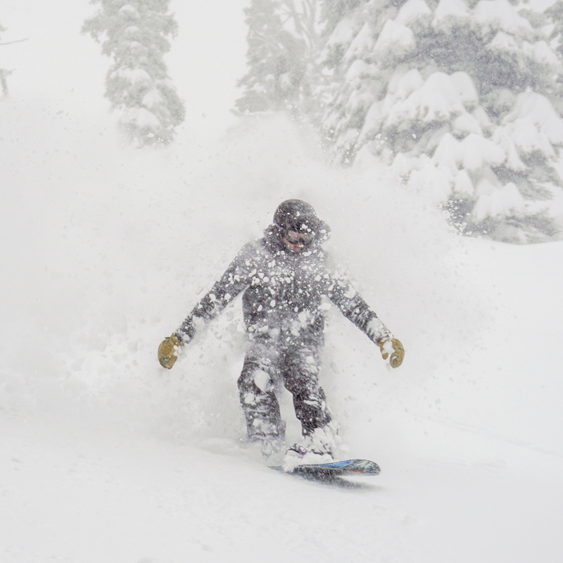 A snowboarder descends the Alah Trail at Mission Ridge Ski Area, spraying a plume of fresh snow in the air.