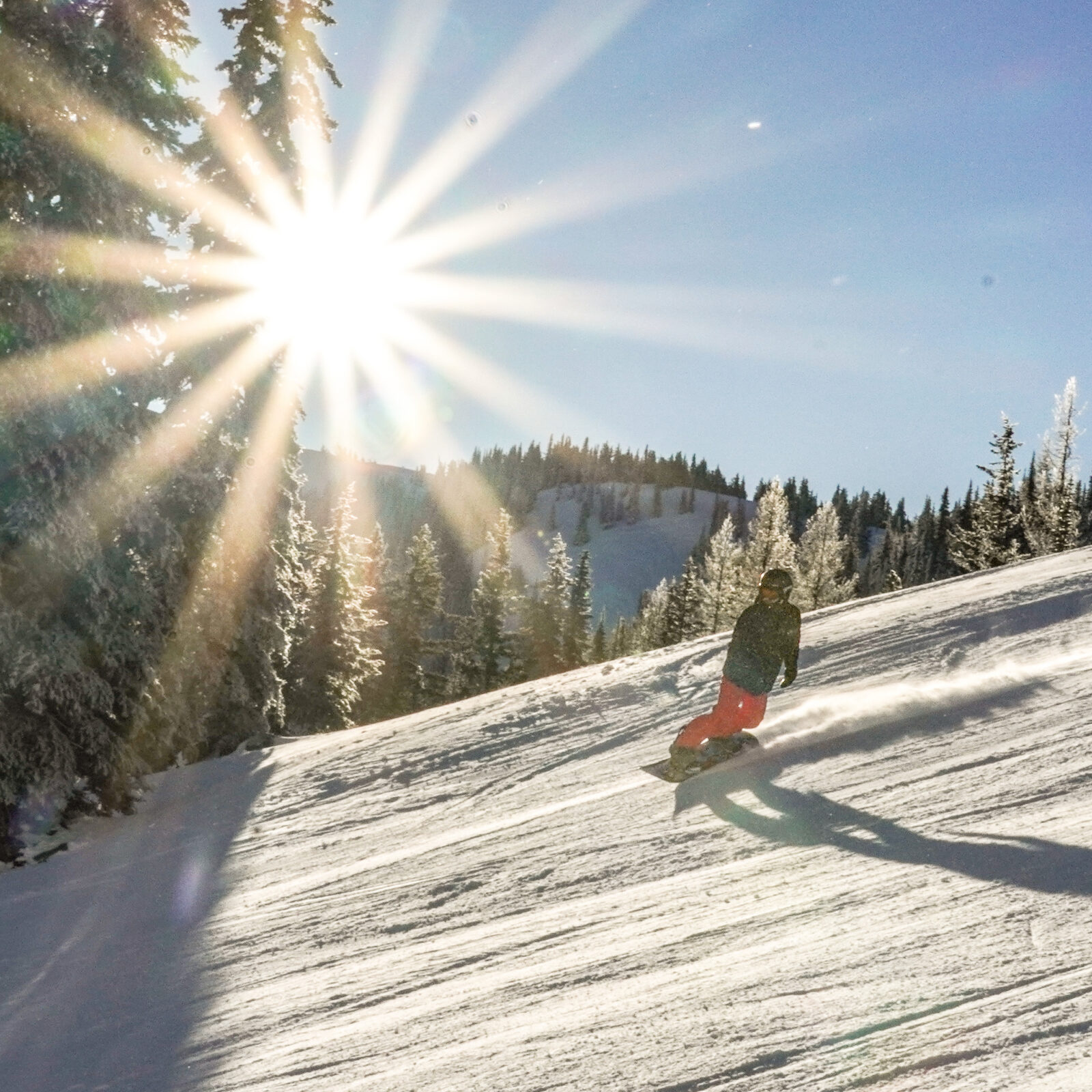 Snowboarder making turn on Bomber Bowl at Mission RIdge with sunburst behind.