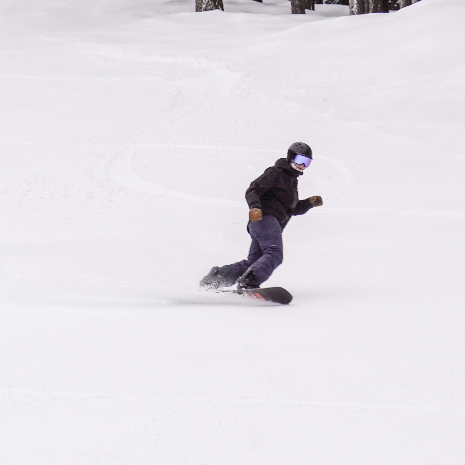 Snowboarder in black making powder turn at Mission Ridge.
