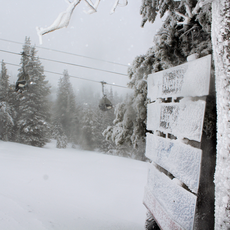 a rimey sign points to snowy ski runs under lift line