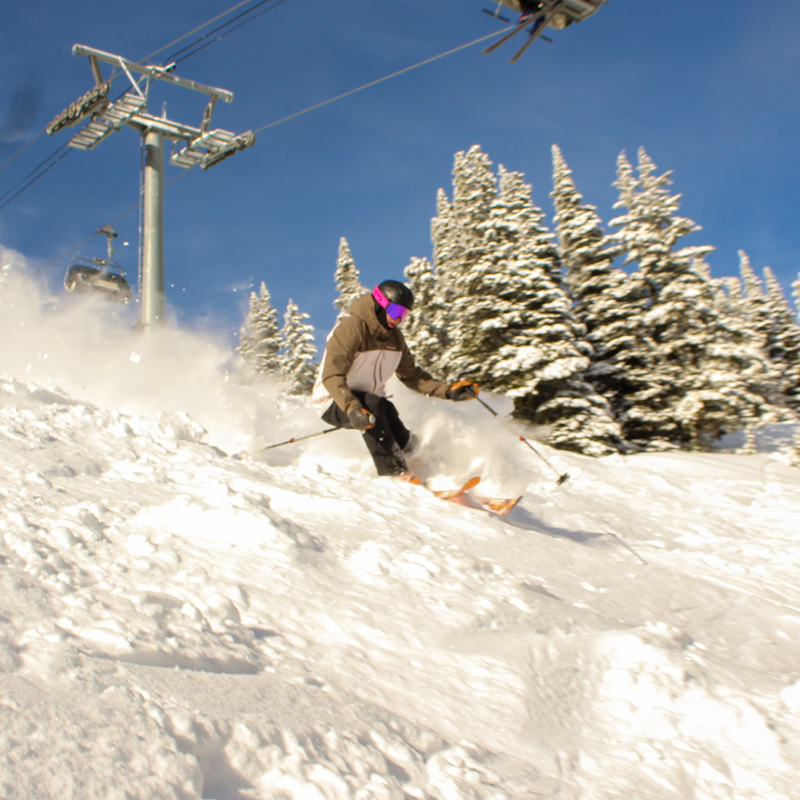 a male skier sprays powder below a lift line