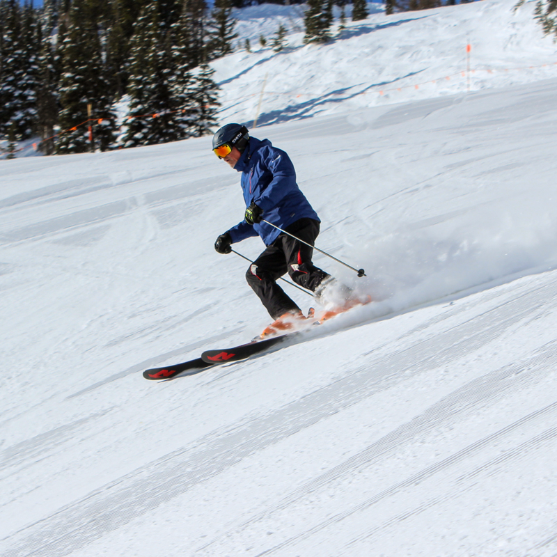 a male skier turns on a sunny groomer