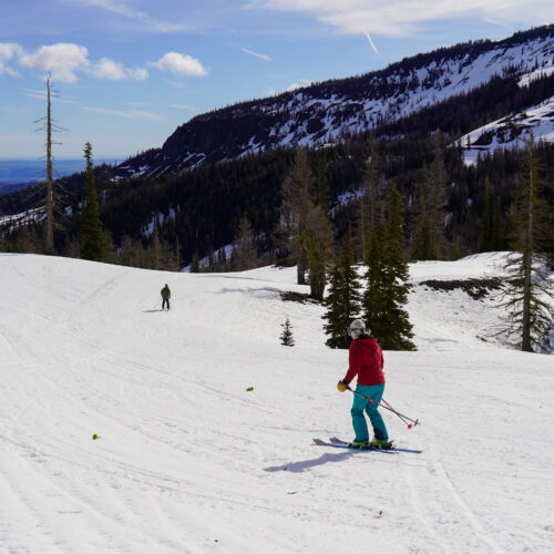 A couple skiers descend a sunny spring slope