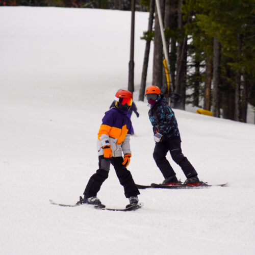 Two young skiers descend the Tumwater trail at Mission Ridge, with some trees in the background.
