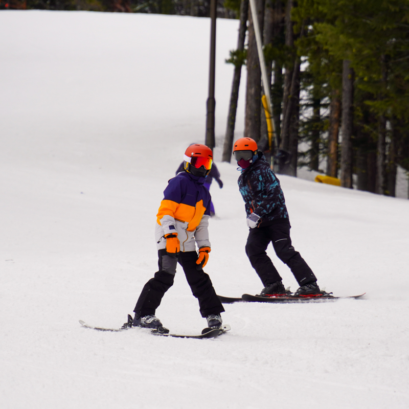 Two young skiers descend the Tumwater trail at Mission Ridge, with some trees in the background.