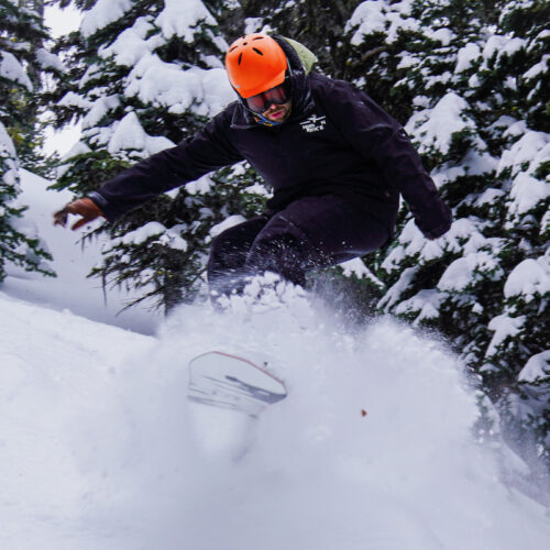 A snowboarder blasts through a powder stash at Mission Ridge. He is wearing a black jacket and orange helmet.